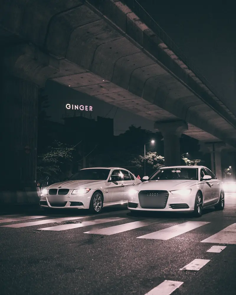 White BMW and Audi A6 side by side at a crossing under the metro viaduct