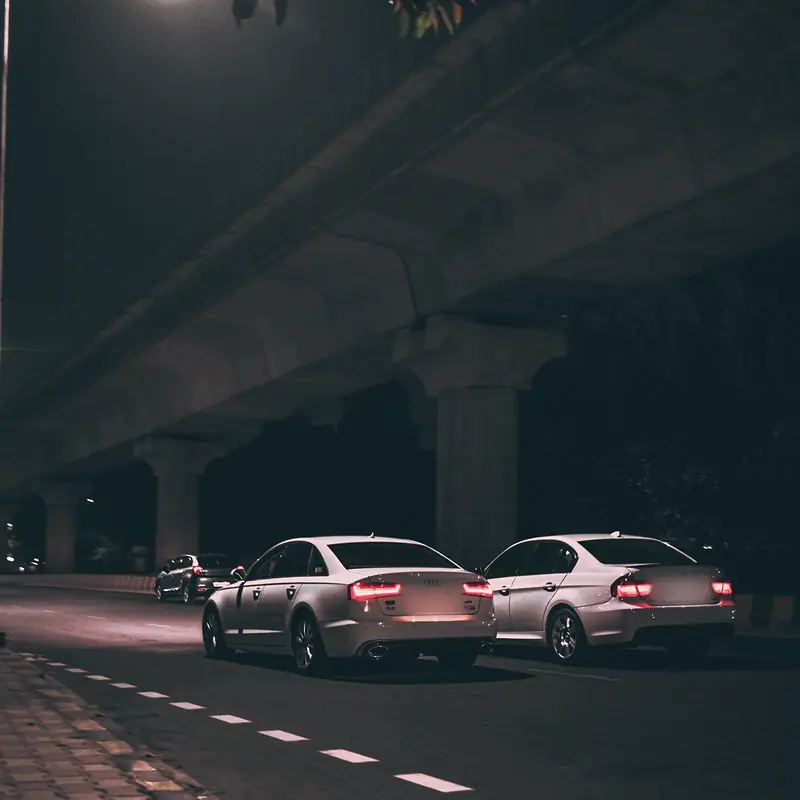 Two white saloons beneath the curve of a metro viaduct at night