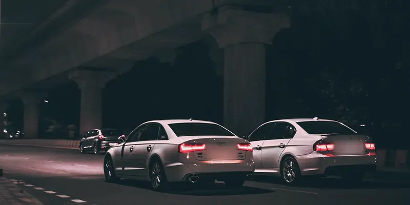 White Audi A6 and BMW tail lights glowing under a metro viaduct at night