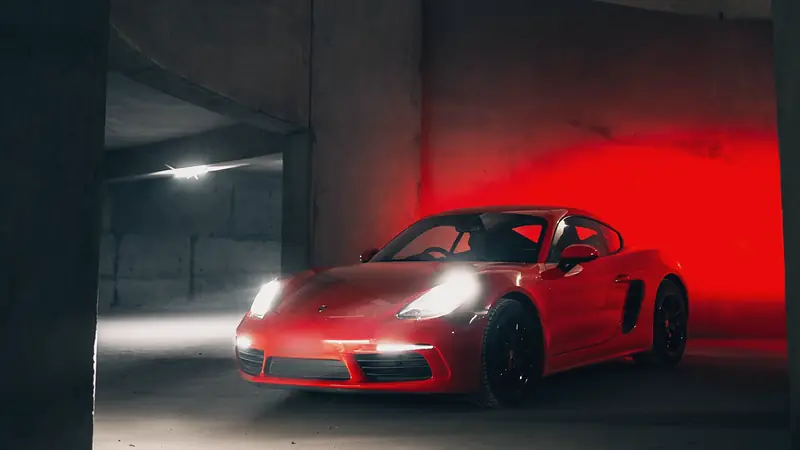 Red Porsche 718 Cayman, headlights on, in a spiral concrete car park