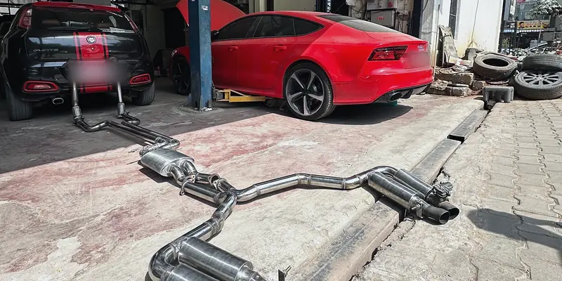 Hand-built stainless exhaust system laid out in front of a red Audi RS7 on the lift