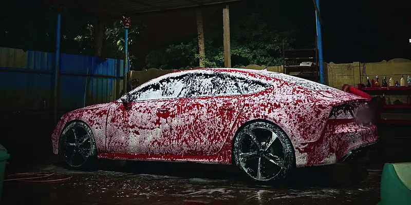 Red Audi RS7 covered in snow foam in the wash bay at night